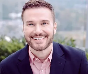 CUWE Conductor Jason Noble smiles at the camera in front of a serene background.